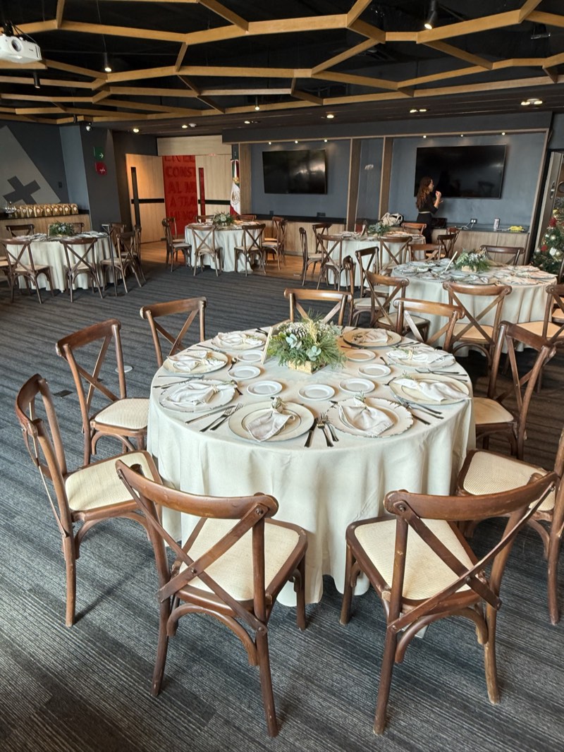 Banquete con sillas crossback de madera, platos base dorados y centros de mesa naturales en el salón de eventos de Bistro 702